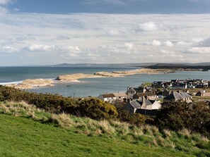 A coastal village with houses near the sea, a grassy foreground, and a clear sky.