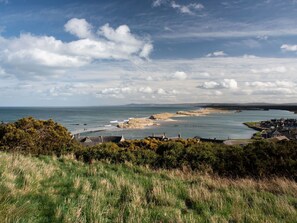 A coastal town with a sea view, grassy areas, and a bridge leading to the beach.