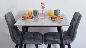 Un comedor con una mesa dispuesta para el desayuno, incluyendo croissants y jugo de naranja, y un cuadro con una imagen de un faro en la pared.