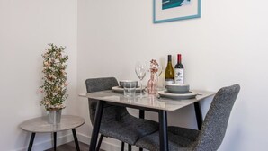 A dining area with a table set for two, featuring a framed picture of a lighthouse, a small potted plant, and a bottle of wine.