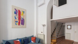 Ein Wohnzimmer mit einem blauen Modulsofa, einem farbenfrohen abstrakten Gemälde, einer Treppe und einer Heizung.