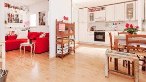 Um apartamento moderno com sofá vermelho, mesa de jantar de madeira e cozinha com armários brancos.