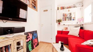 Uma sala de estar com um sofá vermelho, uma mesa de centro, uma estante de livros e uma televisão de tela plana.