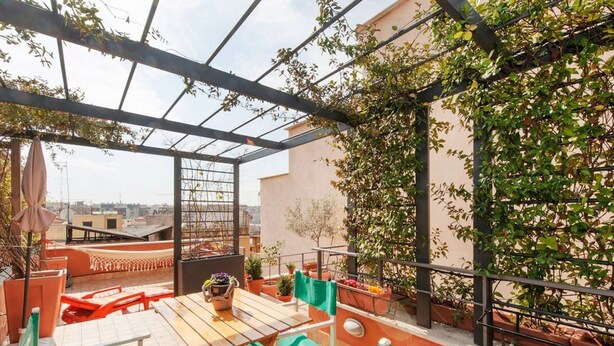 Terraço no telhado com mesa e cadeiras, plantas em vasos e vista panorâmica da cidade.