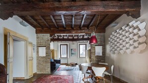 Ein rustikales Interieur mit sichtbaren Holzbalken, einer Steinwand, einem roten Teppich mit Muster, einem Esstisch mit Stühlen und einem einzigartigen Wandkunstwerk.