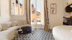 Ein Hotelzimmer mit einer Couch, einem runden Tisch, einem Bett und Blick auf die Stadtlandschaft durch das Fenster.