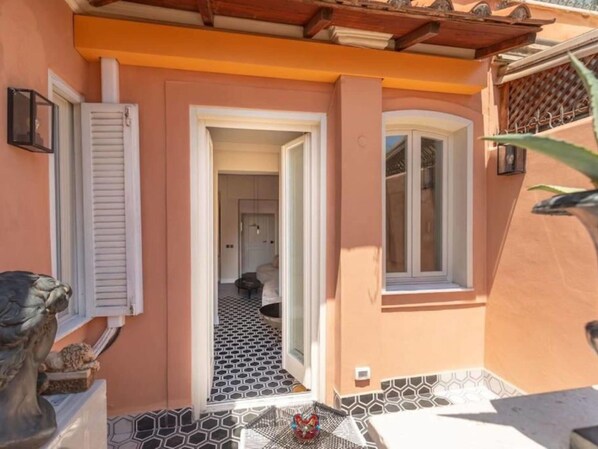 A narrow entrance with a tiled floor leading to a room with a bed and a chair.