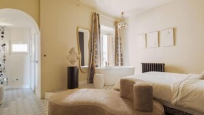 Ein Schlafzimmer mit einem Bett, einem runden Hocker, einem Spiegel und einer Heizung.