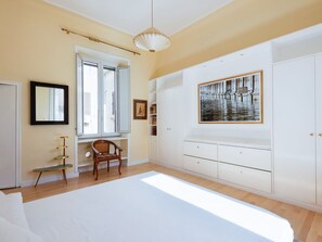 A bedroom with a large bed, a window with blinds, a chair, a wardrobe, and a painting on the wall. - Cosy apartment for 4 guests with A/C, WIFI and TV (Rome)