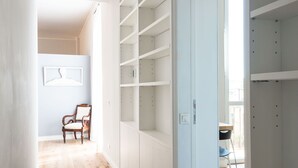 Ein geräumiges Zimmer mit Holzboden, einem weißen Kleiderschrank mit vielen Fächern, einem Sessel und einem kleinen Tisch.