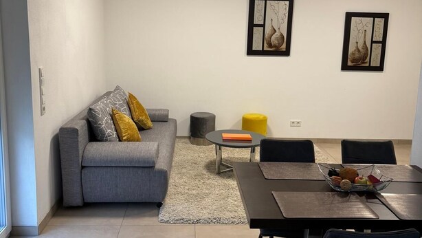 A modern living room with a grey sofa, yellow cushions, a dining table with chairs, and two framed artworks on the wall. - Beautiful apartment in a quiet neighborhood (Maxhütte-Haidhof)
