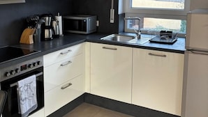 A modern kitchen with white cabinets, a black countertop, a built-in oven, a microwave, and a window with a view of a house. - Beautiful apartment in a quiet neighborhood (Maxhütte-Haidhof)