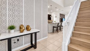 A modern kitchen with a dining area, a staircase, and a decorative wall with geometric patterns.