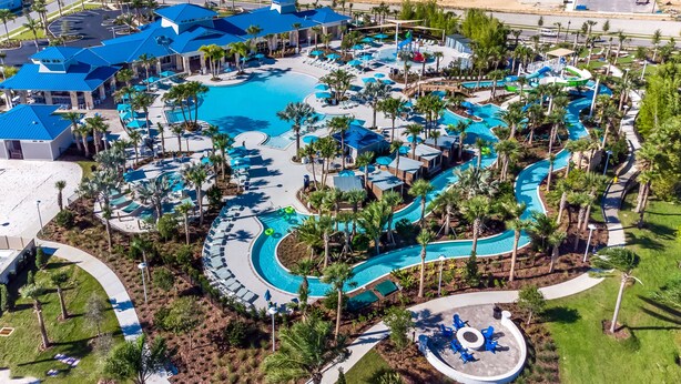 An aerial view of a resort with a large central pool, multiple smaller pools, and a water slide.