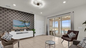 A modern living room with a white console table, two brown armchairs, a glass coffee table, and a large painting of a beach scene.