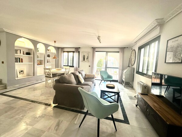 Un salón amplio con sofá, sillas, una mesa de comedor y un balcón con vistas.