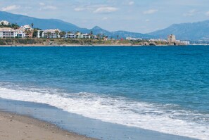 Vista costera con playa, océano y edificios al fondo.