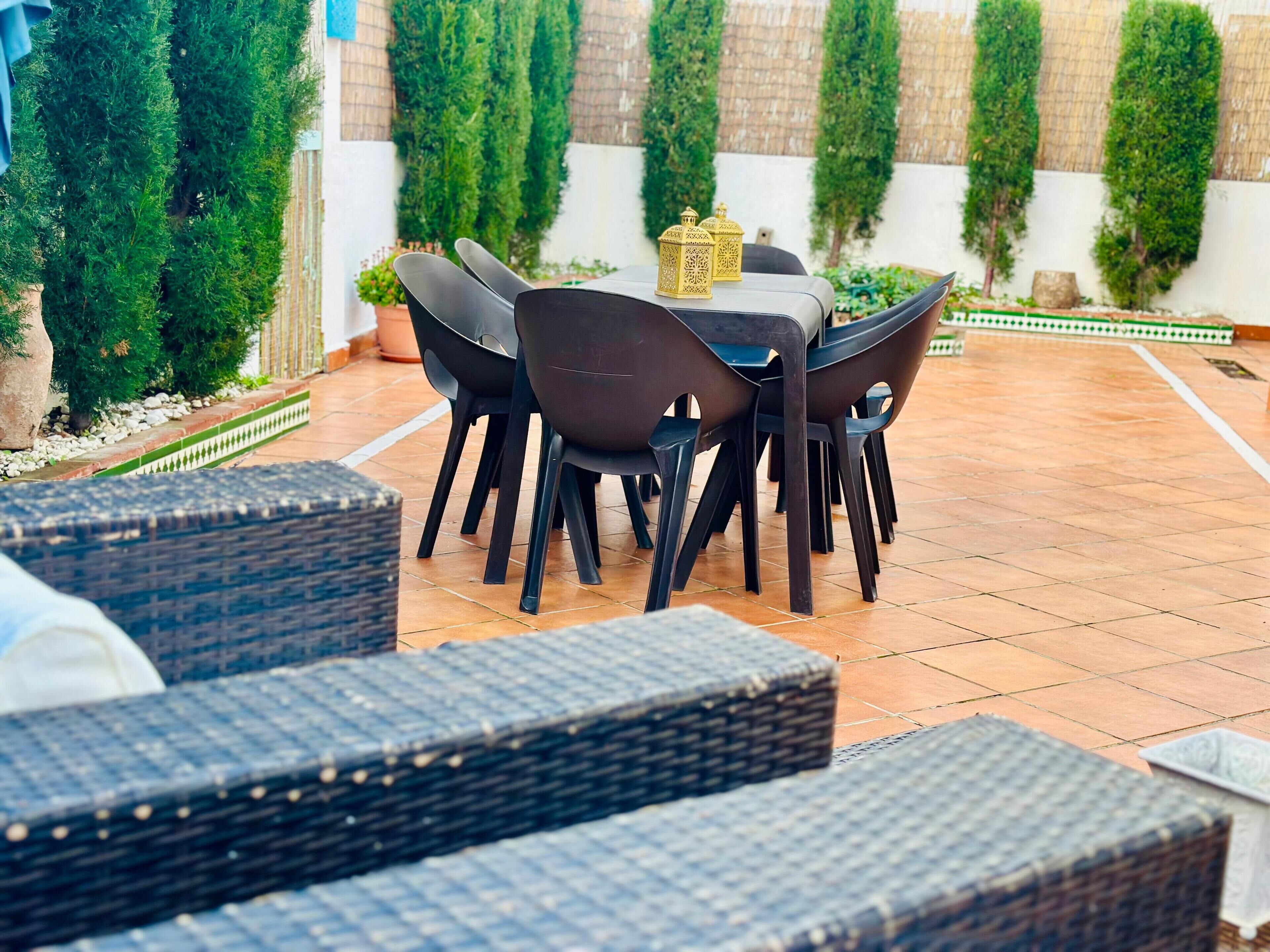 Un espace patio avec une table ronde et des chaises, entouré de plantes en pot et agrémenté d’une lanterne décorative.