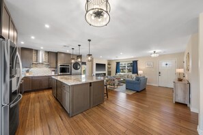 Una cocina moderna con una isla central, electrodomésticos de acero inoxidable y una zona de comedor con un sofá azul y una lámpara.