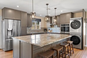 Una cocina moderna con electrodomésticos de acero inoxidable, una isla de mármol e iluminación colgante.