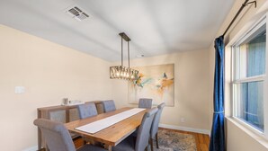 Un comedor con una mesa de madera, sillas tapizadas en gris, una lámpara colgante y una ventana con cortinas.