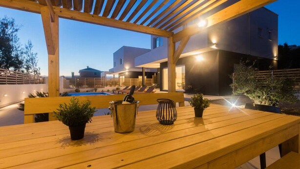 Una pérgola de madera al aire libre con zona de piscina, bancos y plantas en macetas.
