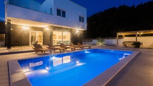 Una casa moderna de dos pisos con piscina, zona de estar exterior y un patio bien iluminado.
