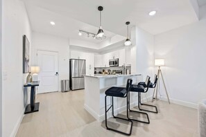 Una cocina moderna con armarios blancos, electrodomésticos de acero inoxidable y una isla central con taburetes de bar.