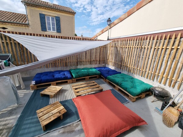 A rooftop terrace with wooden benches, colorful cushions, and a large shade sail. - Full Appart / 4 bedrooms, 4 bathrooms, Terrace, Garage, Baby Foot (Agen)