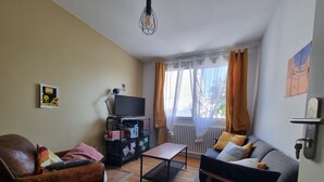 Ein Wohnzimmer mit einem braunen Ledersessel, einem grauen Sofa, einem Couchtisch aus Holz und einem Fernseher auf einem Lowboard.