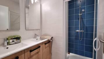 Un bagno moderno con lavandino bianco, mobili in legno, uno specchio e zona doccia rivestita di piastrelle blu.