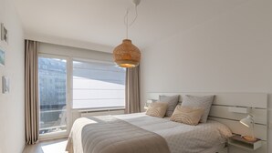 Una camera da letto con un letto grande, un comodino con una lampada, un lampadario e una finestra con tende.