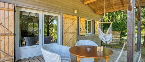 A wooden deck with wicker furniture, a hanging hammock, and a glass door leading to a covered area.