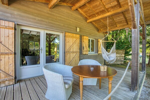 A wooden deck with wicker furniture, a hanging hammock, and a glass door leading to a covered area.