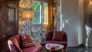 Ett rum med ett träpanelat tak, ett stort fönster med gardiner, ett träskåp, två fåtöljer och ett litet bord med en lampa.