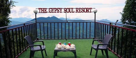 Un balcón con una mesa lista para dos personas, con vistas a un paisaje montañoso.