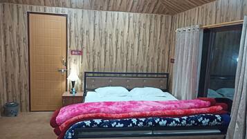 Un dormitorio con paneles de madera en la pared, una cama con varias almohadas, una mesita de noche con lámpara y un ventanal con cortinas.