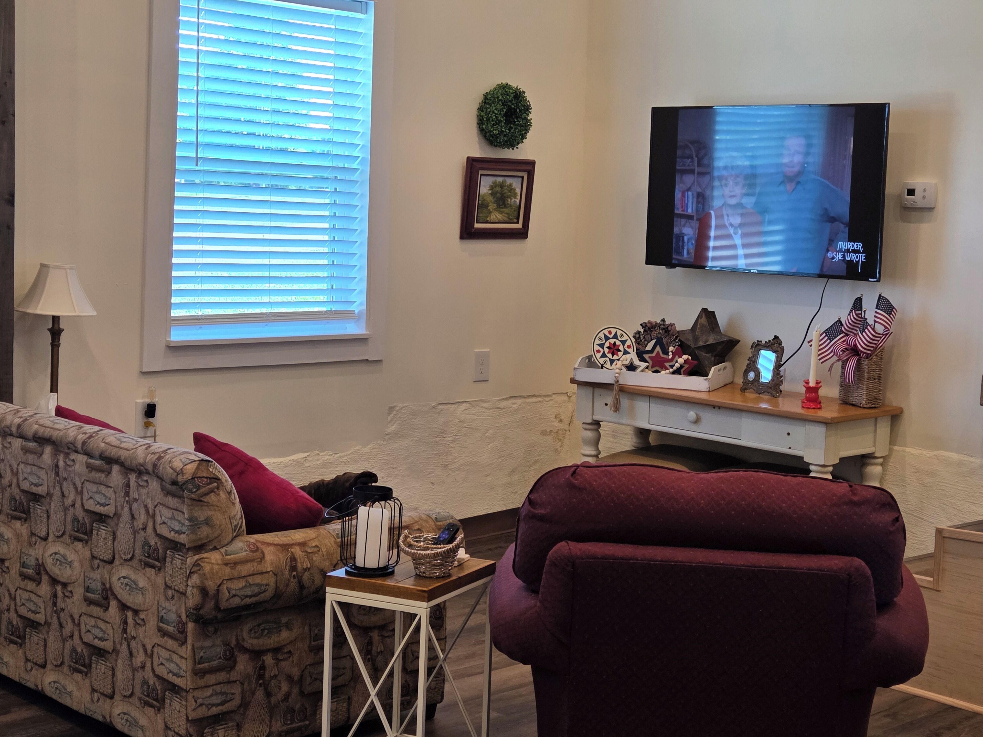 Un salon comprenant un canapé, un téléviseur, une petite table agrémentée d’objets décoratifs et une fenêtre avec des stores.
