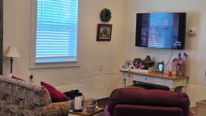 A living room with a sofa, a television, a small table with decorative items, and a window with blinds. - Charming historic barn in New Market with WiFi and AC (New Market)