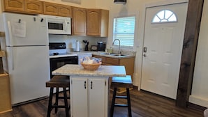 A kitchen with wooden cabinets, a refrigerator, a microwave, a sink, and a window with blinds. - Charming historic barn in New Market with WiFi and AC (New Market)