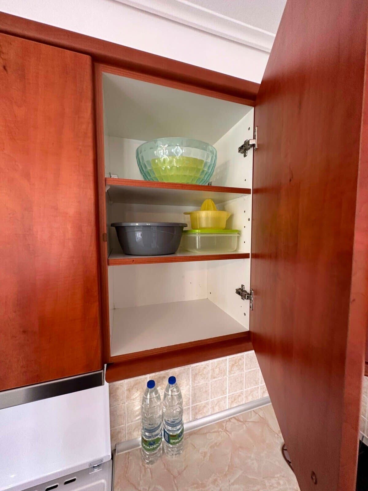 A kitchen with wooden cabinets, a glass bowl, a yellow container, a gray pot, and two water bottles.