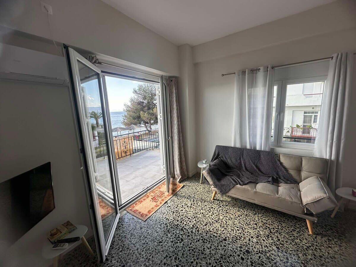 Quarto com sofá, televisão, mesa pequena e janela com cortinas.