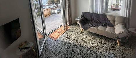 Quarto com sofá, televisão, mesa pequena e janela com cortinas.