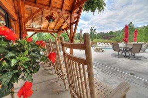 A wooden outdoor seating area with chairs and tables, a pool in the background, and a view of the surrounding landscape. - Heaven's Hideaway - 2 King Suites/Pet Friendly/Hot Tub/Firepit (Sevierville)