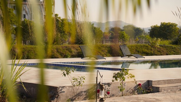 A swimming pool with lounge chairs, a concrete deck, and a small garden area with a lantern. - Ranthambore Village Serai (Sawai Madhopur)