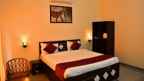 A hotel room with a bed, a nightstand, a chair, a wall-mounted air conditioner, a wall-mounted light, and a framed picture of a zebra. - Ranthambore Village Serai (Sawai Madhopur)