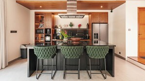 A modern kitchen with a central island, bar stools, wooden ceiling beams, and built-in appliances.