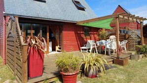 Een rode houten woning met een grijs dak, een overdekte patio met witte plastic stoelen en potplanten.