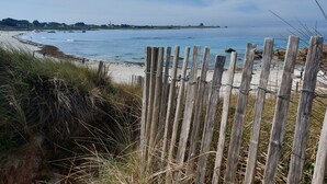 Een strand met een houten hek op de voorgrond, een zandstrand en de zee op de achtergrond.