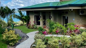 Un edificio con techo verde, rodeado de un jardín con diversas plantas y un camino que lleva a la entrada.